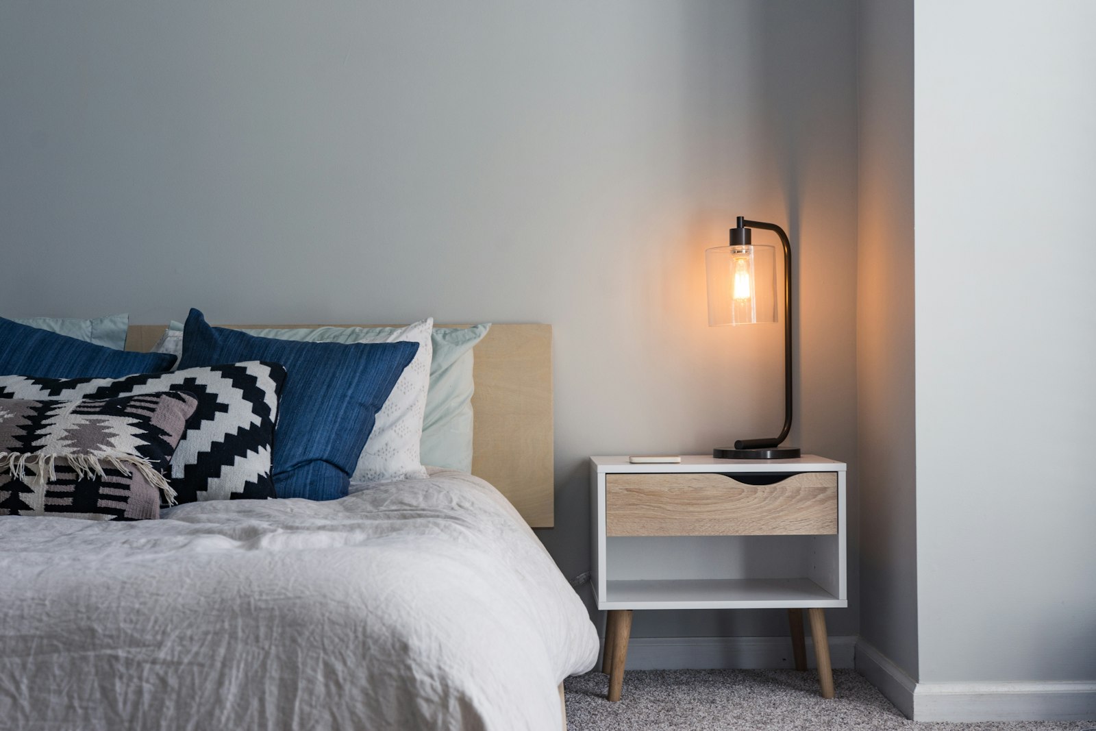 Bedside lamp glowing beside a made bed